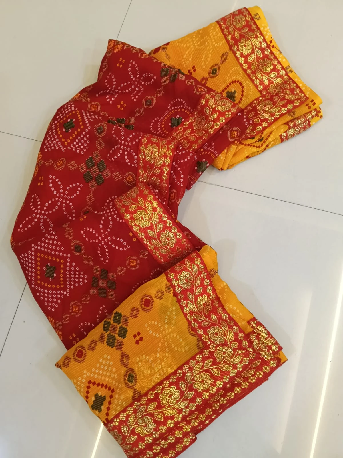 Folded red and yellow silk saree with gold floral border and traditional woven motifs