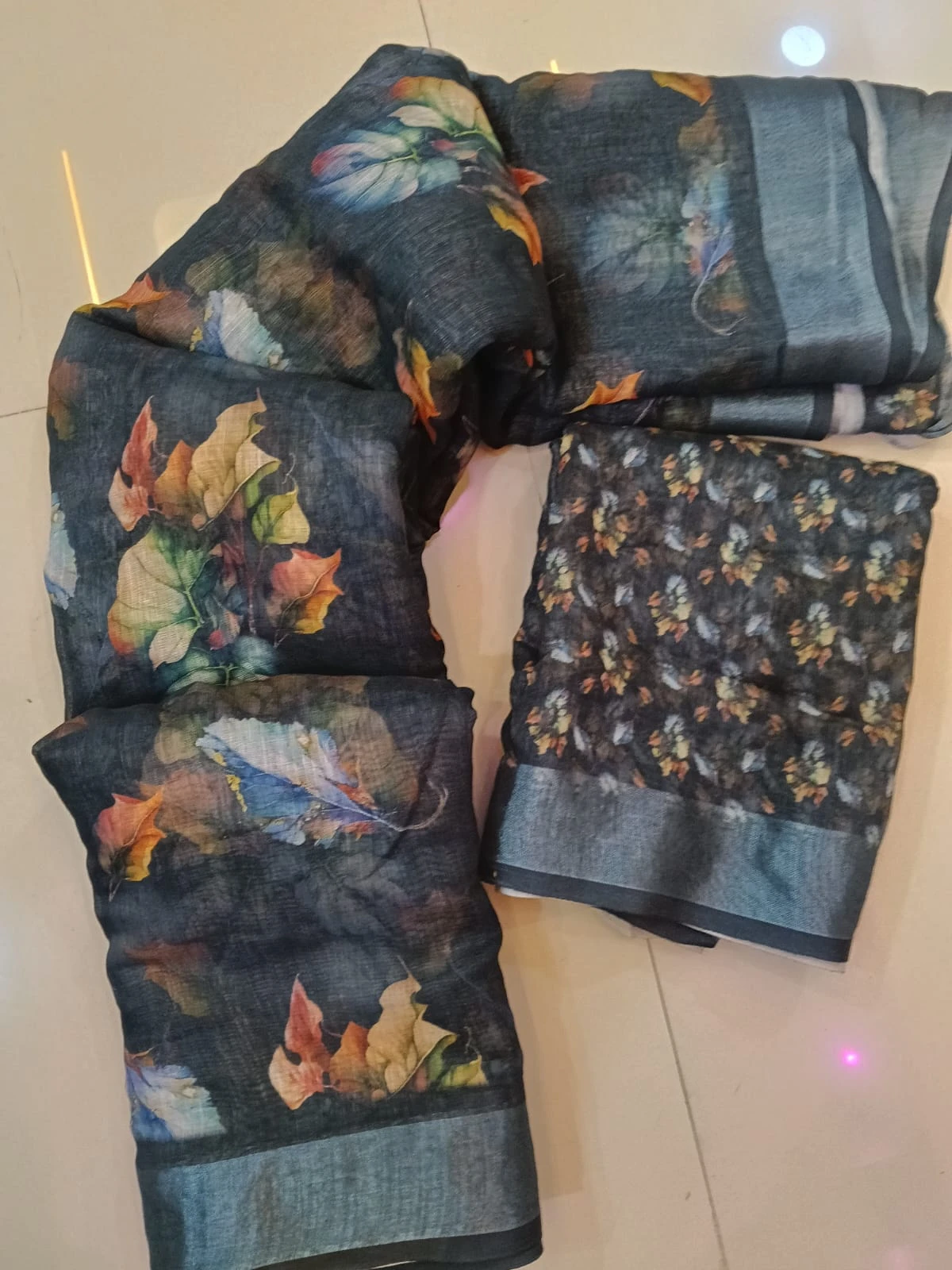 Dark floral printed saree fabric with matching blouse piece laid on a tiled floor
