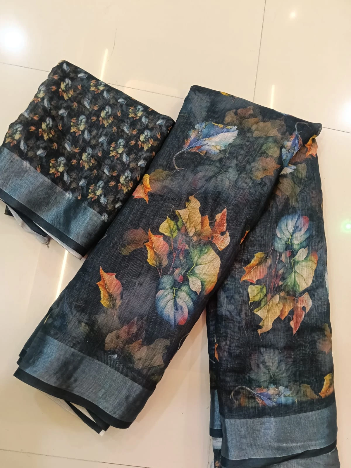 Dark floral printed saree fabric with matching blouse piece laid on a tiled floor