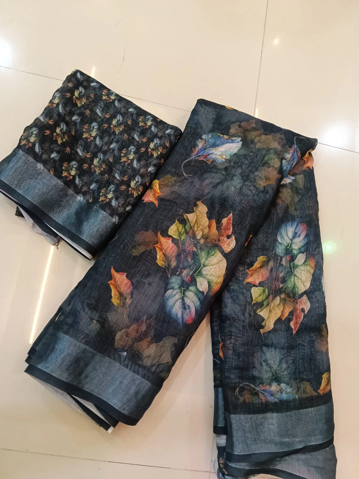 Dark floral printed saree fabric with matching blouse piece laid on a tiled floor