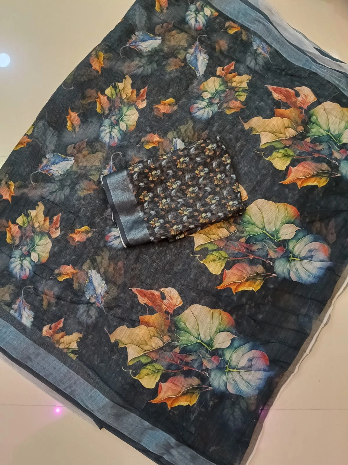 Dark floral printed saree fabric with matching blouse piece laid on a tiled floor